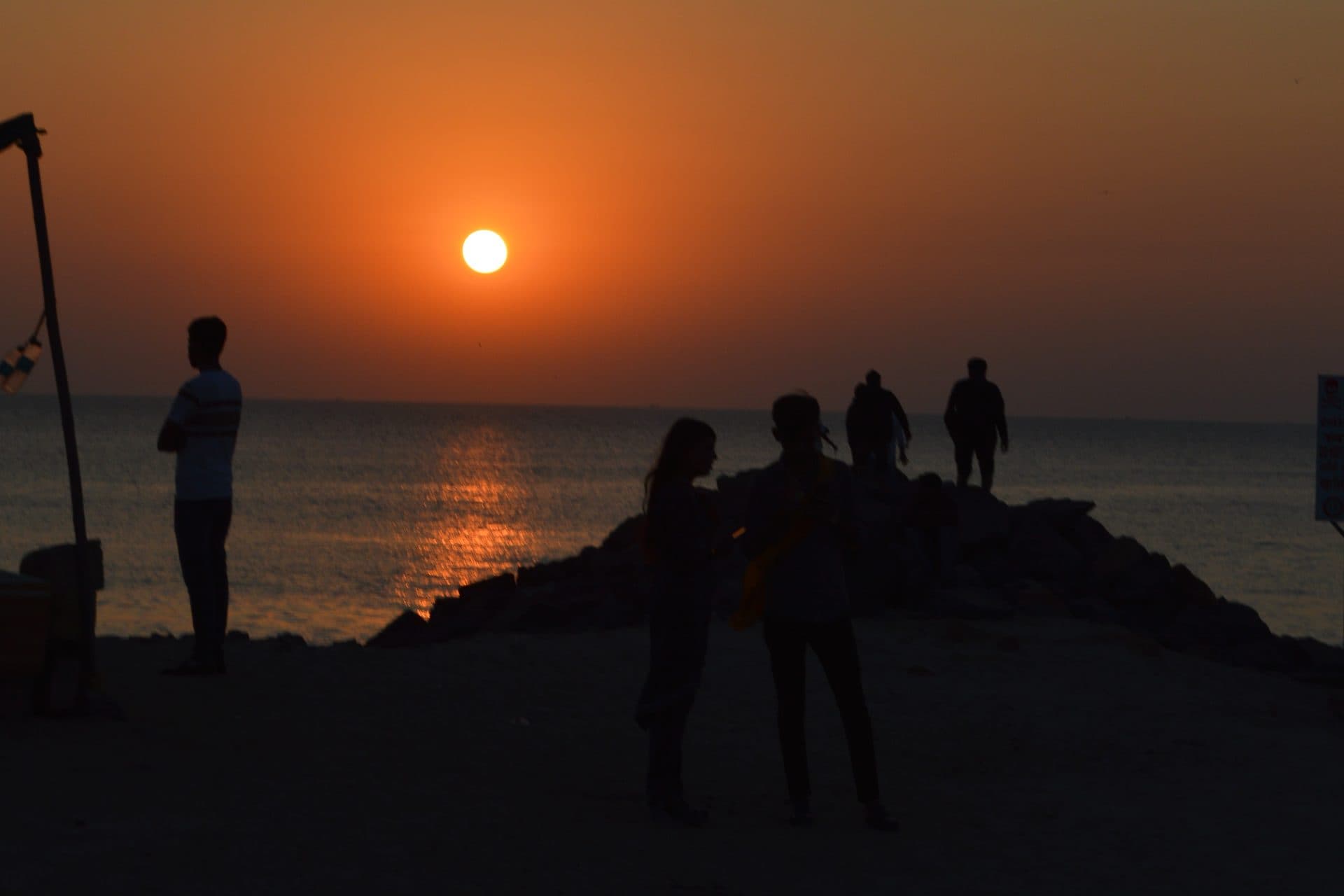 Silhouettes of people gathered beside the sea at sunset